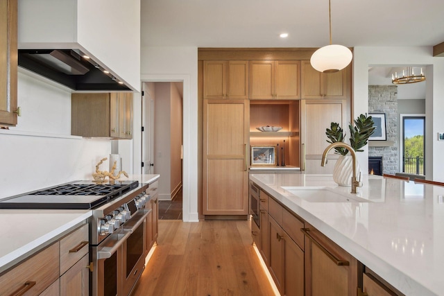 kitchen with a fireplace, range with two ovens, light hardwood / wood-style floors, decorative light fixtures, and range hood