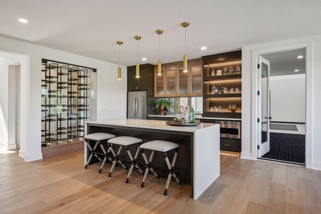 bar with light hardwood / wood-style floors, appliances with stainless steel finishes, a textured ceiling, and pendant lighting