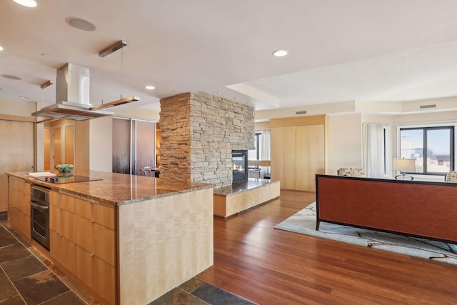 kitchen with a stone fireplace, stone counters, dark wood-type flooring, stainless steel oven, and a center island