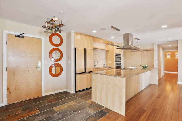 kitchen featuring light stone counters, light brown cabinets, island exhaust hood, dark wood-type flooring, and built in fridge