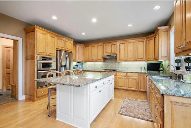 kitchen featuring light wood-type flooring, a kitchen island, sink, light stone counters, and stainless steel appliances