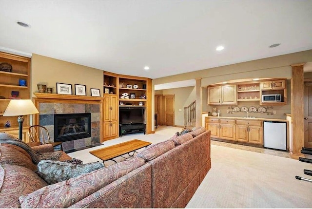 carpeted living room featuring a fireplace, built in shelves, and sink