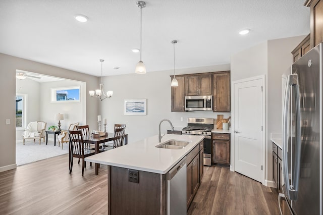 kitchen with wood-type flooring, a center island with sink, sink, hanging light fixtures, and appliances with stainless steel finishes