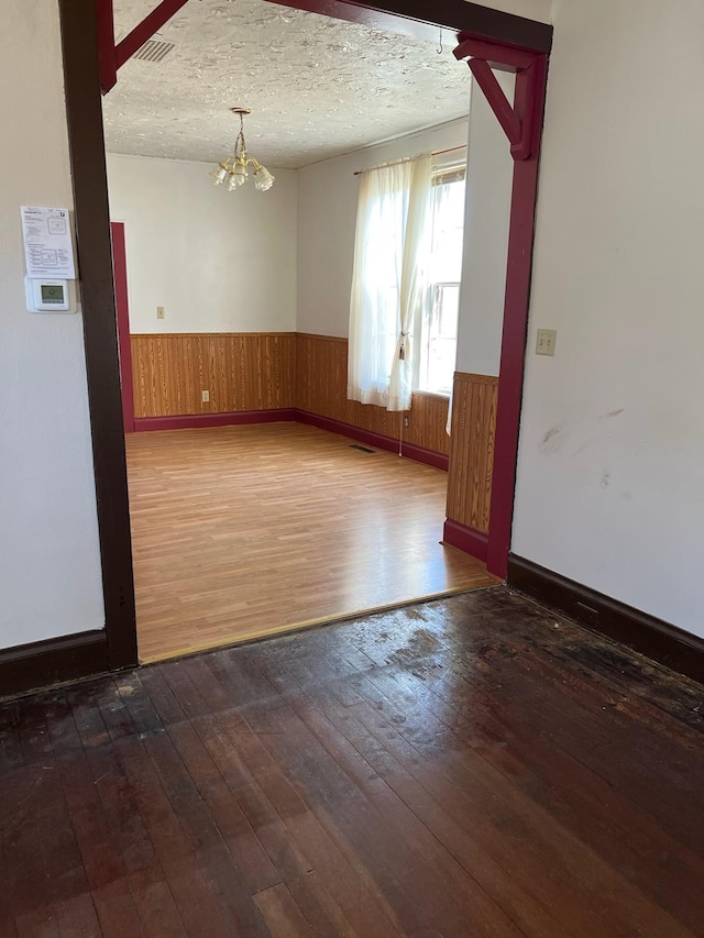 721 5th Ave E, Alexandria, MN 56308 - empty room with dark wood finished floors, a wainscoted wall, a chandelier, wooden walls, and a textured ceiling