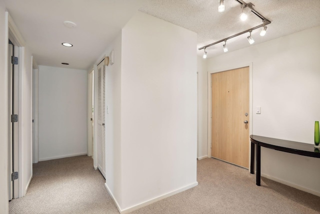 corridor featuring rail lighting, light colored carpet, and a textured ceiling