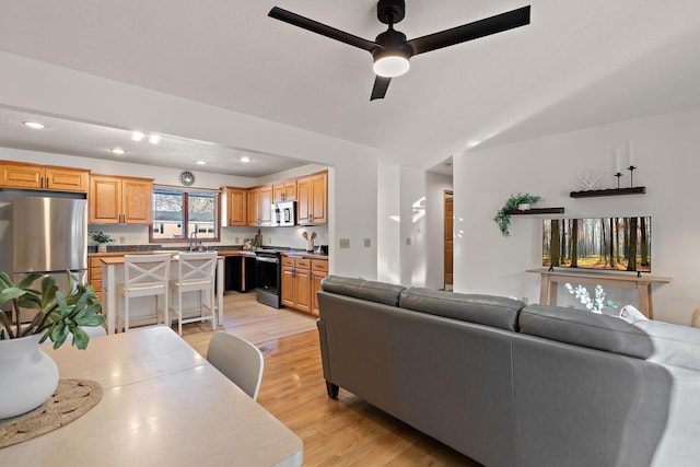 living room with sink, light hardwood / wood-style floors, and ceiling fan