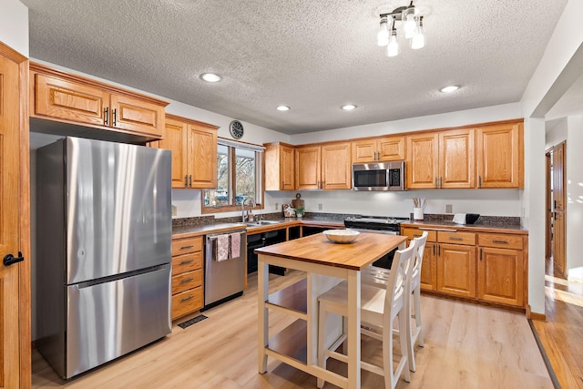 kitchen with appliances with stainless steel finishes, sink, a textured ceiling, and light wood-type flooring