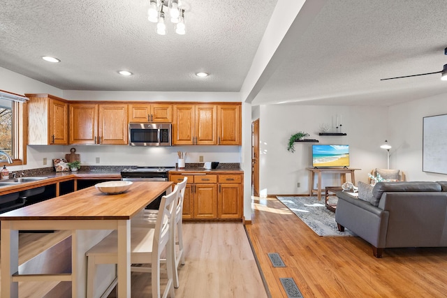 kitchen featuring wood counters, sink, a textured ceiling, ceiling fan, and light hardwood / wood-style floors