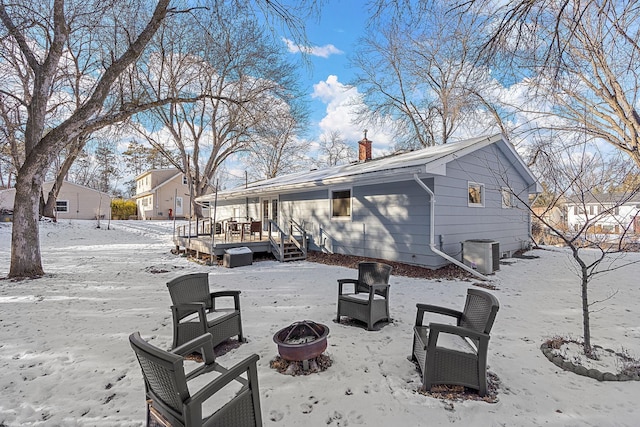 snow covered back of property with a wooden deck, a fire pit, and cooling unit