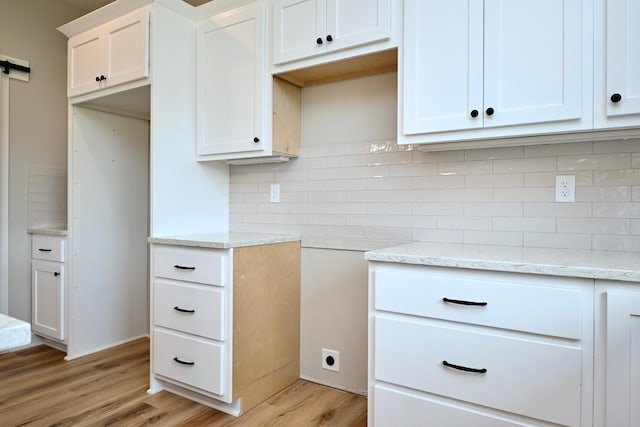 kitchen featuring white cabinetry, light stone counters, light wood-type flooring, and backsplash