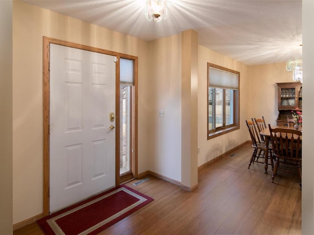 foyer entrance with a notable chandelier, a textured ceiling, baseboards, and wood finished floors