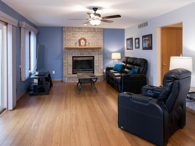 living area featuring visible vents, light wood-style floors, a brick fireplace, ceiling fan, and baseboards