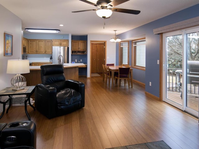 living room with ceiling fan with notable chandelier, baseboards, and wood finished floors