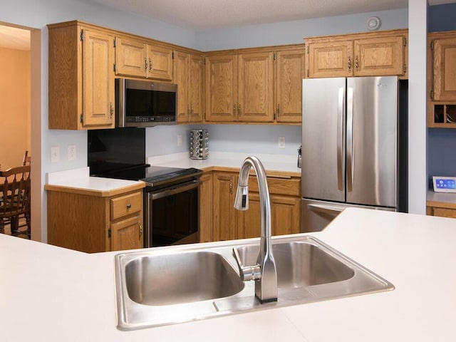 kitchen featuring light countertops, appliances with stainless steel finishes, a sink, and brown cabinets