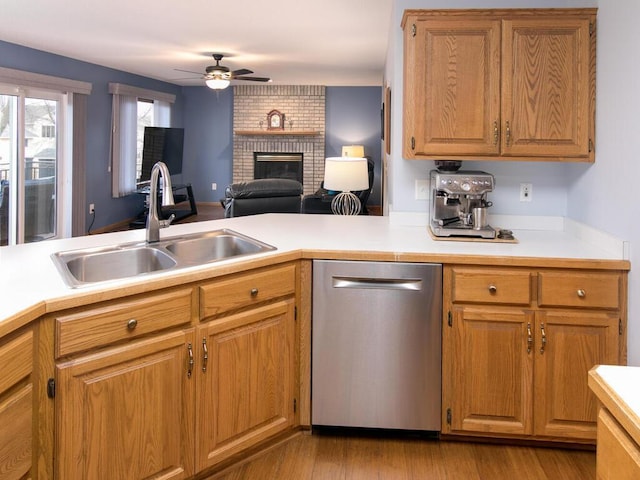 kitchen with ceiling fan, a fireplace, a sink, light countertops, and stainless steel dishwasher