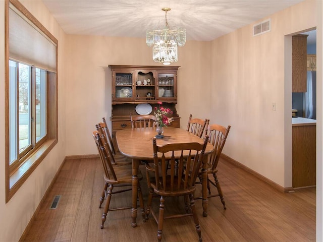 dining area with a chandelier, wood-type flooring, visible vents, and baseboards