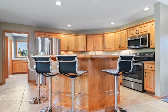 kitchen with appliances with stainless steel finishes, light tile patterned flooring, a kitchen island, and a kitchen breakfast bar