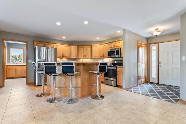 kitchen featuring light brown cabinets, a breakfast bar area, light tile patterned floors, a kitchen island, and stainless steel appliances