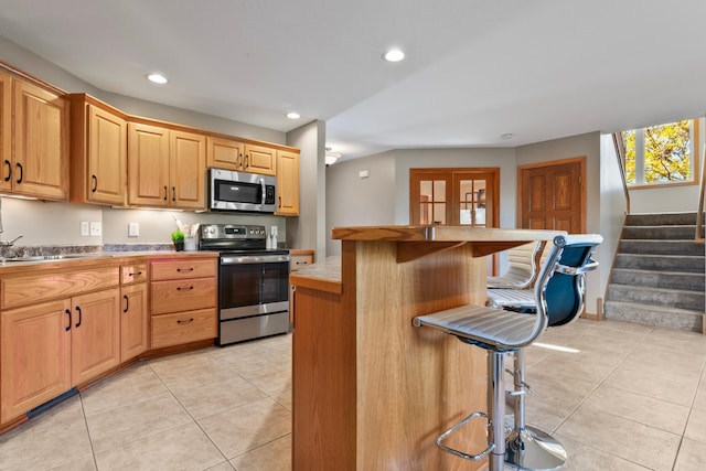 kitchen featuring a kitchen island, a breakfast bar area, light tile patterned flooring, french doors, and stainless steel appliances