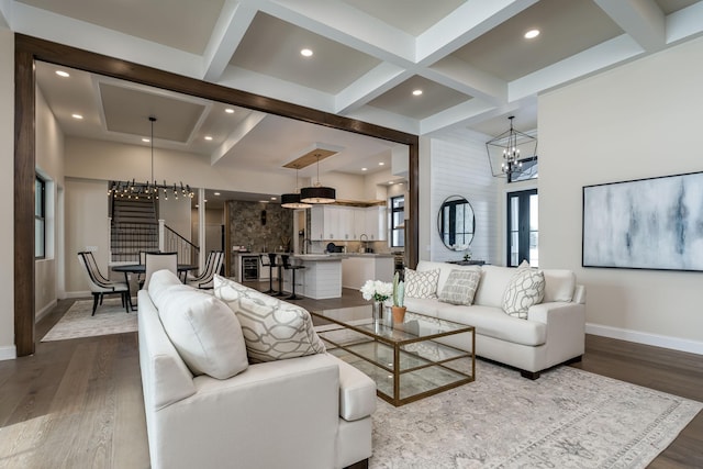 living room with hardwood / wood-style flooring, coffered ceiling, an inviting chandelier, and beam ceiling