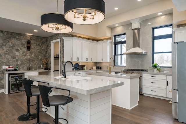 kitchen featuring white cabinetry, decorative light fixtures, appliances with stainless steel finishes, an island with sink, and beverage cooler