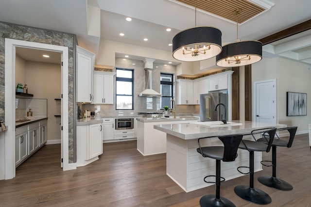 kitchen with pendant lighting, tasteful backsplash, white cabinetry, a kitchen island with sink, and wall chimney range hood