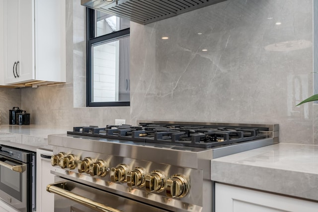 kitchen featuring backsplash, high end stainless steel range, light stone countertops, and white cabinets