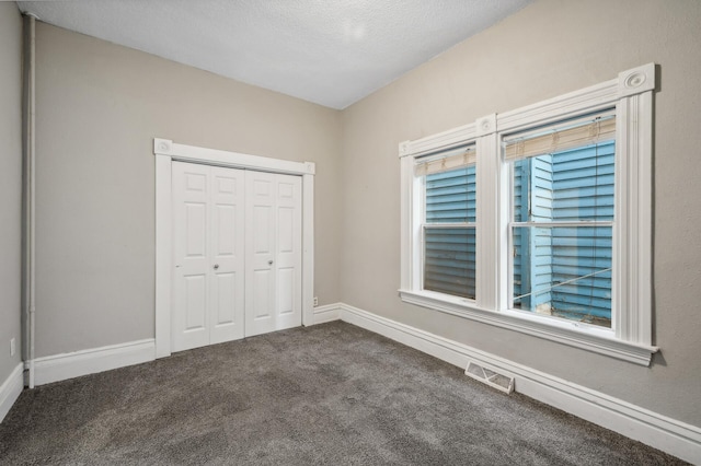 unfurnished bedroom featuring a closet, dark carpet, and a textured ceiling