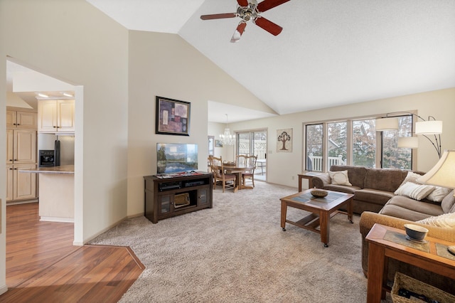 living area featuring light colored carpet, baseboards, high vaulted ceiling, ceiling fan with notable chandelier, and light wood-type flooring