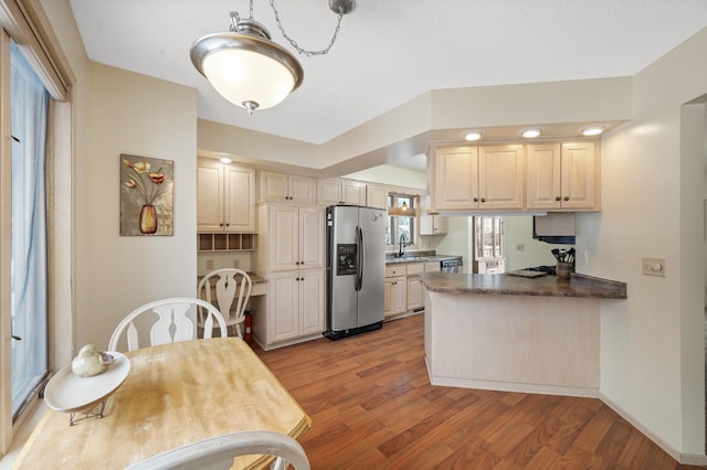 kitchen featuring dark countertops, light wood-type flooring, a peninsula, stainless steel fridge, and a sink