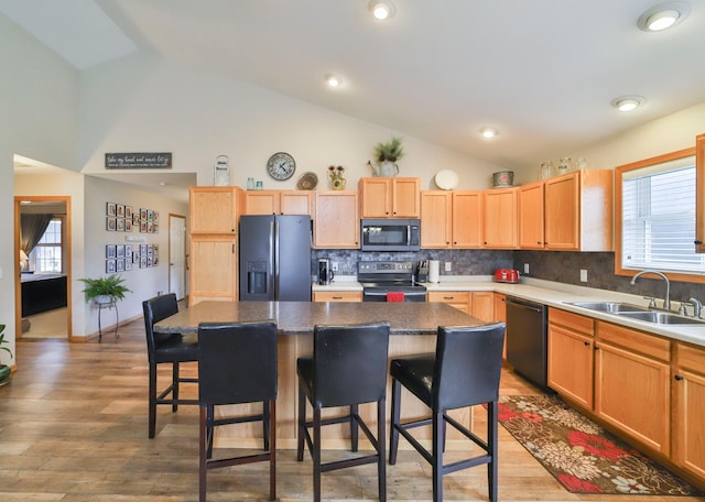 kitchen with vaulted ceiling, sink, a kitchen breakfast bar, a center island, and black appliances