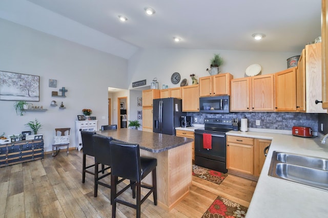 kitchen with a breakfast bar, sink, tasteful backsplash, light hardwood / wood-style flooring, and black appliances