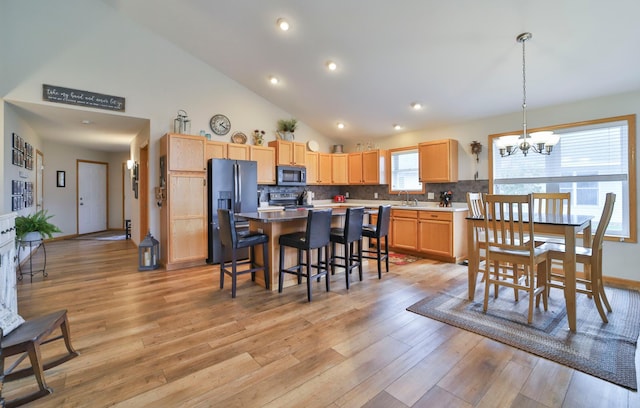 kitchen with an inviting chandelier, backsplash, hanging light fixtures, stainless steel appliances, and light wood-type flooring