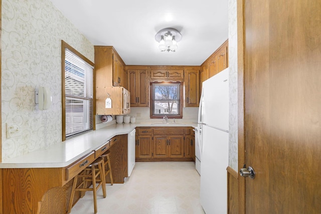 4312 Georgia Ave N, Crystal, MN 55428 - kitchen featuring light floors, wallpapered walls, freestanding refrigerator, a sink, and brown cabinets