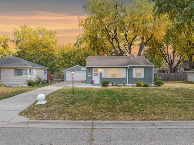 ranch-style house featuring an outbuilding, a lawn, a detached garage, and fence