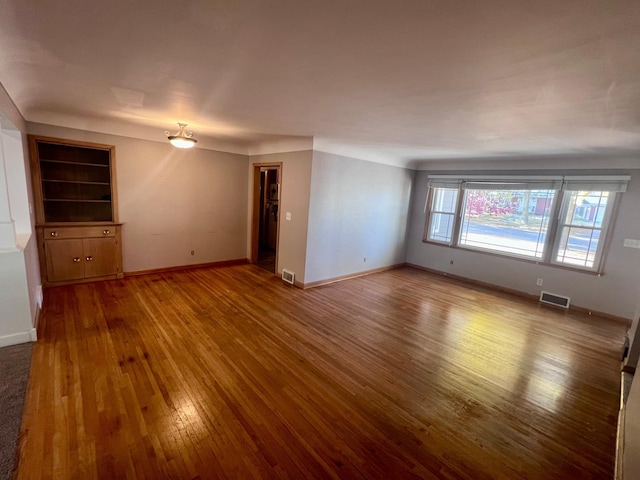 unfurnished living room featuring built in features and hardwood / wood-style floors