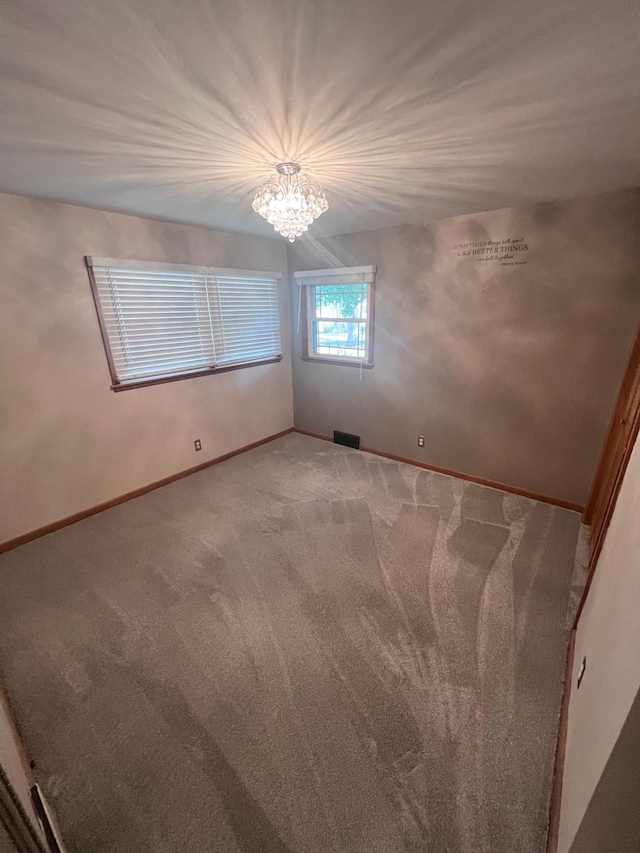 carpeted spare room with an inviting chandelier