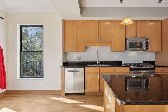 kitchen with dark stone countertops, sink, light hardwood / wood-style floors, appliances with stainless steel finishes, and decorative light fixtures