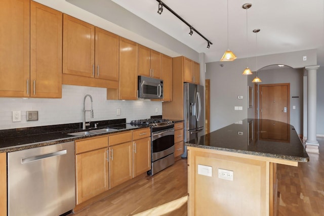 kitchen with hanging light fixtures, sink, stainless steel appliances, decorative columns, and light wood-type flooring