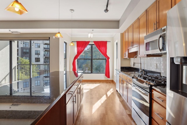 kitchen featuring pendant lighting, sink, backsplash, stainless steel appliances, and light hardwood / wood-style floors