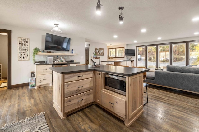 kitchen featuring light brown cabinets, a textured ceiling, decorative light fixtures, a kitchen island with sink, and dark hardwood / wood-style floors