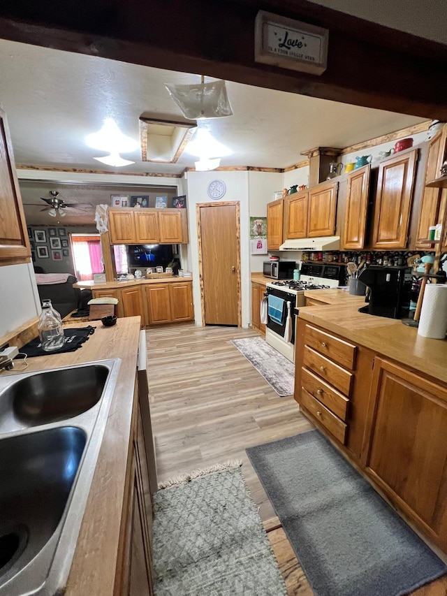 kitchen with white gas range, ceiling fan, crown molding, light hardwood / wood-style flooring, and sink