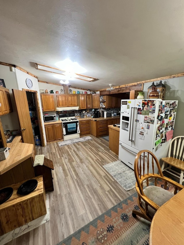 kitchen with a skylight, decorative backsplash, white appliances, and light hardwood / wood-style flooring