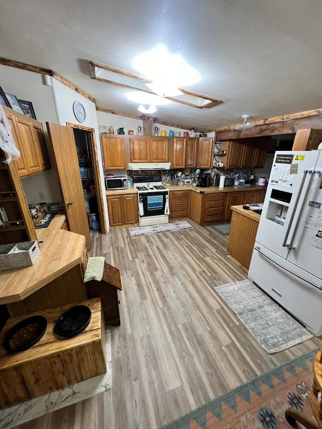 kitchen with decorative backsplash, white appliances, light hardwood / wood-style floors, a skylight, and a textured ceiling