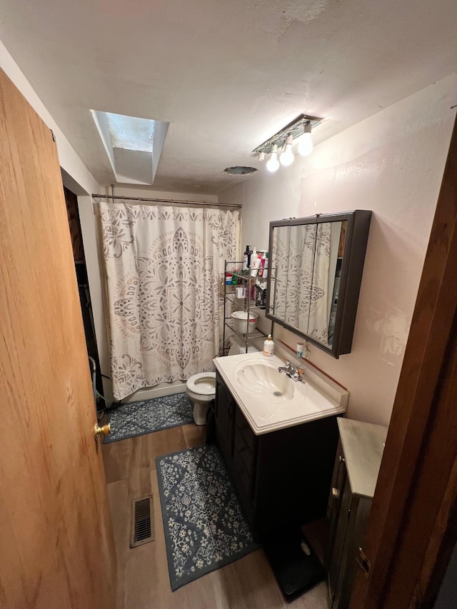 bathroom with a skylight, vanity, toilet, and hardwood / wood-style flooring