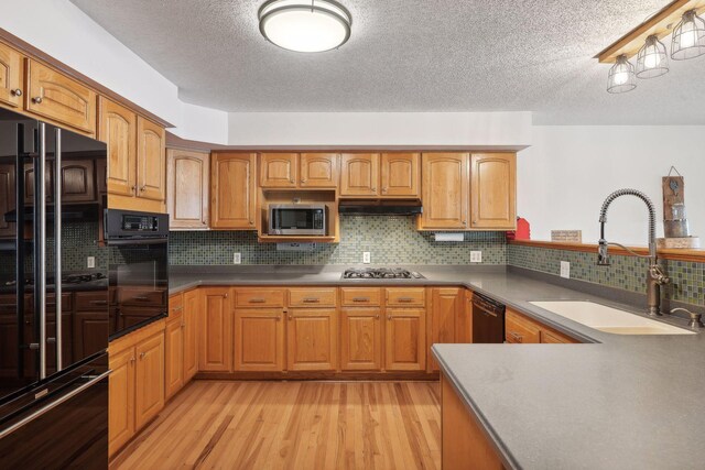 kitchen with light wood-type flooring, black appliances, backsplash, sink, and a textured ceiling