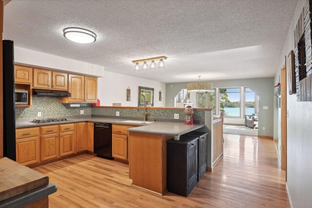 kitchen featuring sink, kitchen peninsula, stainless steel appliances, light wood-type flooring, and decorative backsplash