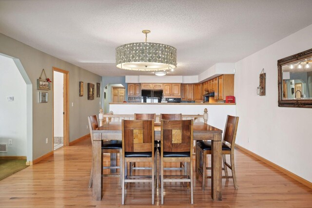 dining space with sink, light hardwood / wood-style floors, an inviting chandelier, and a textured ceiling