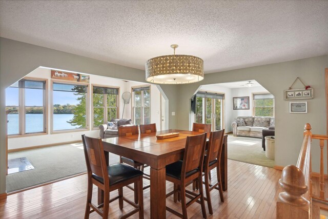 dining room with a textured ceiling, a water view, and light wood-type flooring