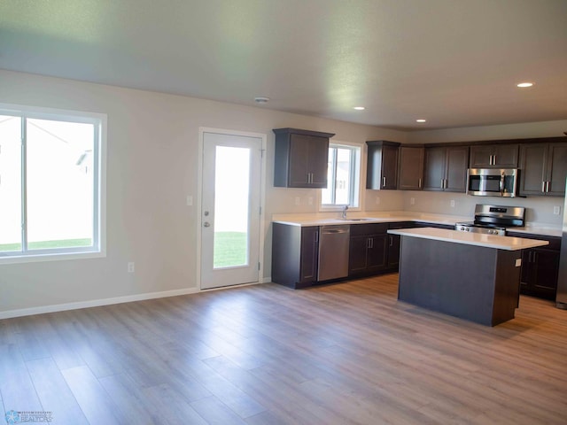 kitchen featuring appliances with stainless steel finishes, light wood-type flooring, dark brown cabinetry, sink, and a kitchen island